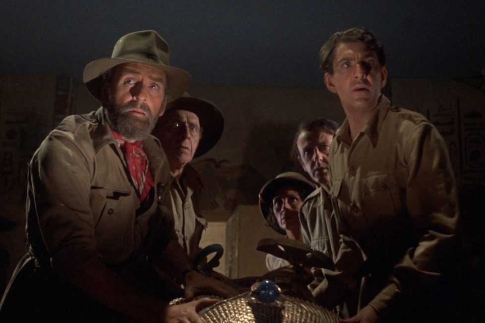 Cena dos arqueólogos na tumba da Rainha Tera em O Túmulo do Sangue. O plano mostra 5 arqueólogos com semblantes assustados ao redor de um sarcófago.