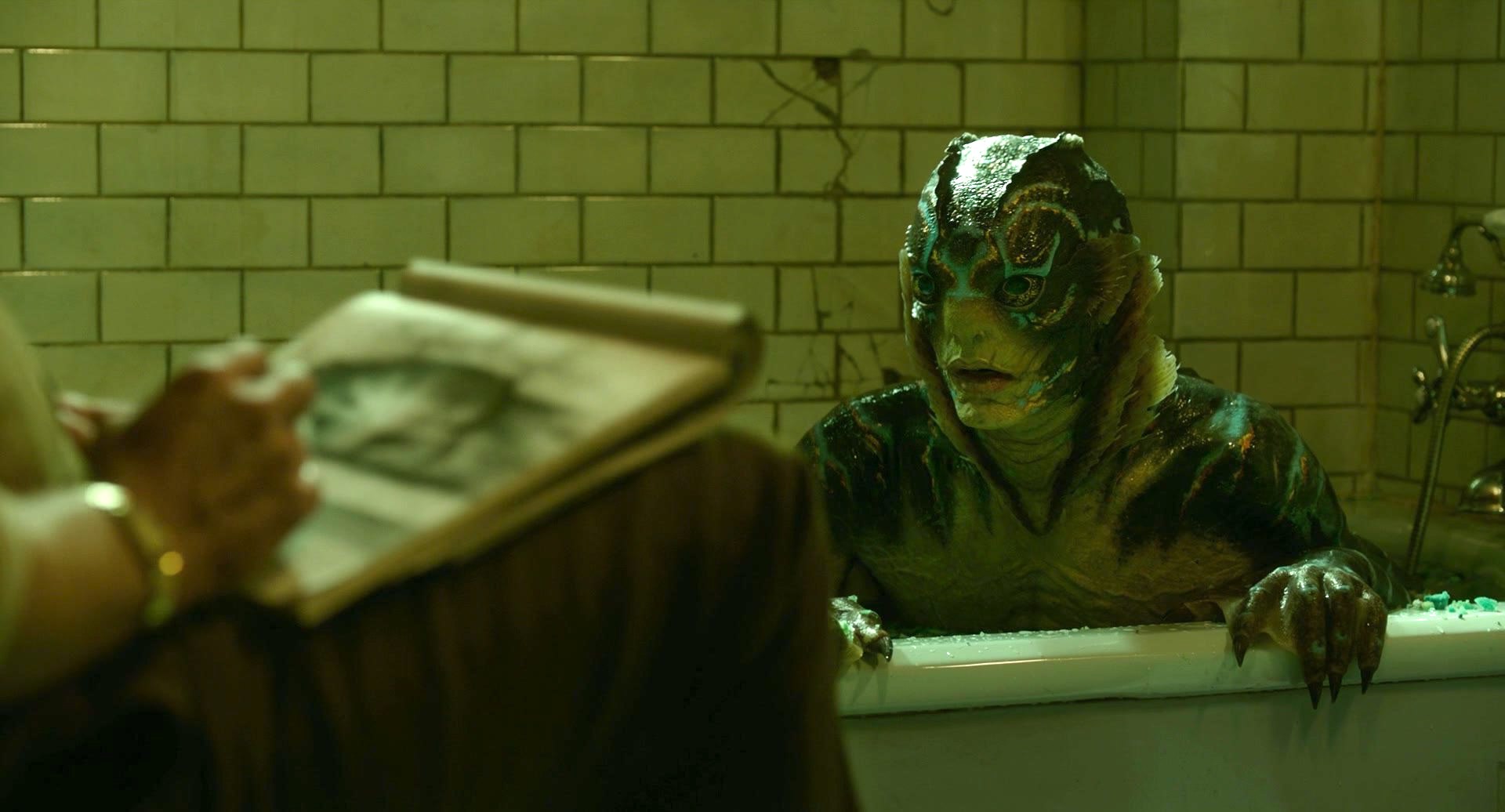 Cena do filme A Forma da Água (2017) mostrando a criatura meio-peixe em uma banheira olhando atenta para alguém fora do plano que está à desenhando.