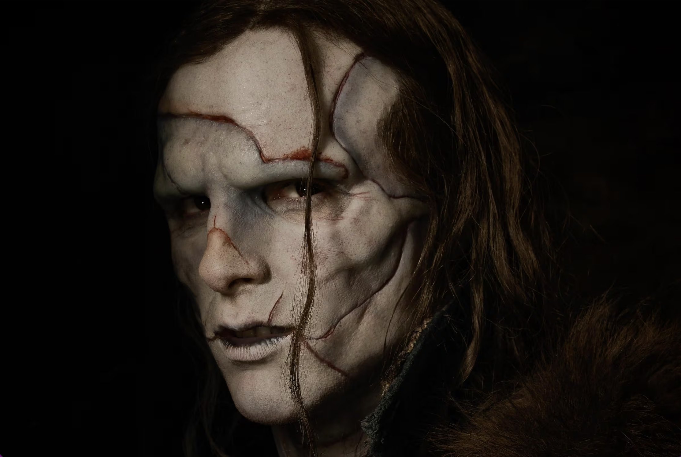 Imagem de divulgação do filme Frankenstein focada no rosto da criatura. Ela tem o rosto magro com marcas de costura de peles, cabelo negro longo e um olhar fixo e sofrido.