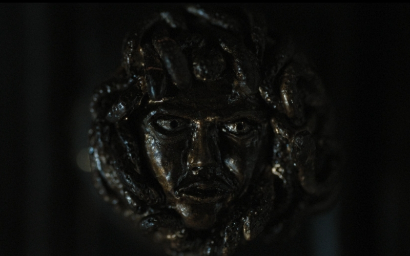 Cena do filme A Primeira Profecia (2024) mostrando um close na maçaneta de uma porta. Na malçaneta está esculpida a cabeça de medusa.