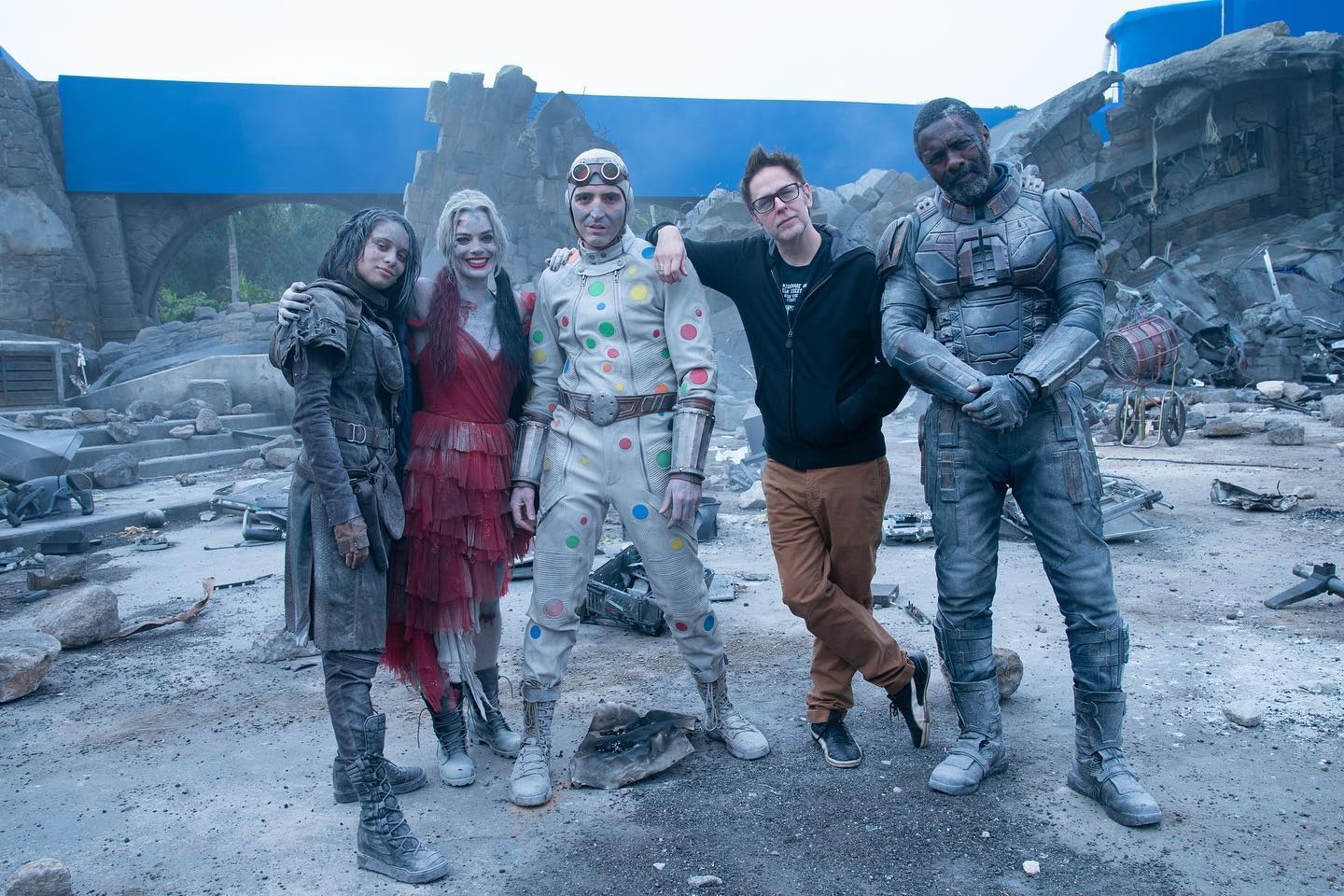 Foto do set de O Esquadrão Suicida (2021) mostrando os atores caracterizados e sujos ao lado de James Gunn. Da esquerda para a direita: A caçadora de ratos (Daniela Melchior), Arlequina (Margot Robbie), Bolinha (David Dastmalchian), James Gunn e Sanguinário (Idris Elba).