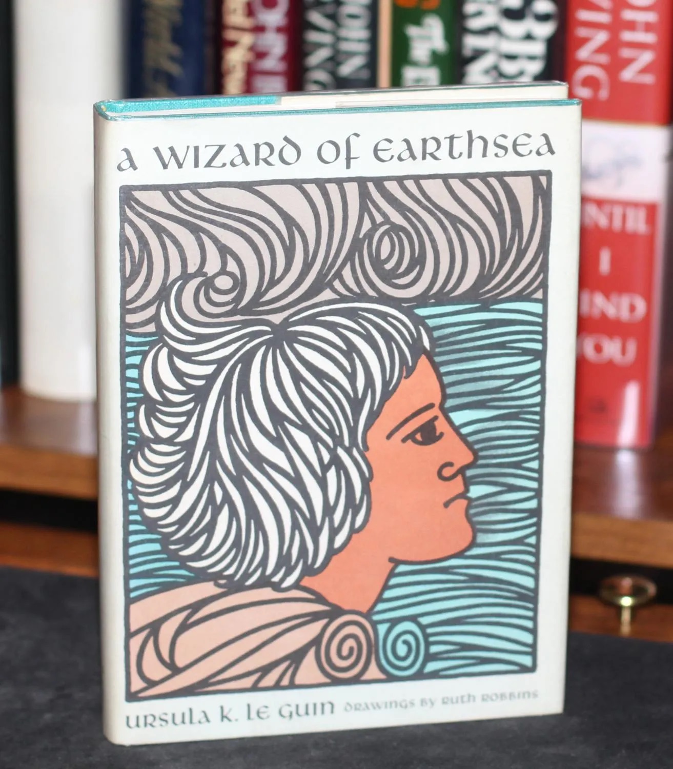 capa de O Feiticeiro de Terramar com ilustração de Ruth Robbins mostrando o rosto de Ged com pele escura em frente ao mar.