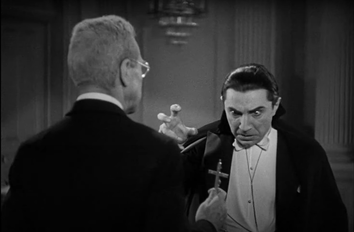 Cena do Filme Drácula de 1931 com Van Helsing mostrando calmamente uma pequena cruz para Drácula, que está paralizado, encarando a cruz com medo.
