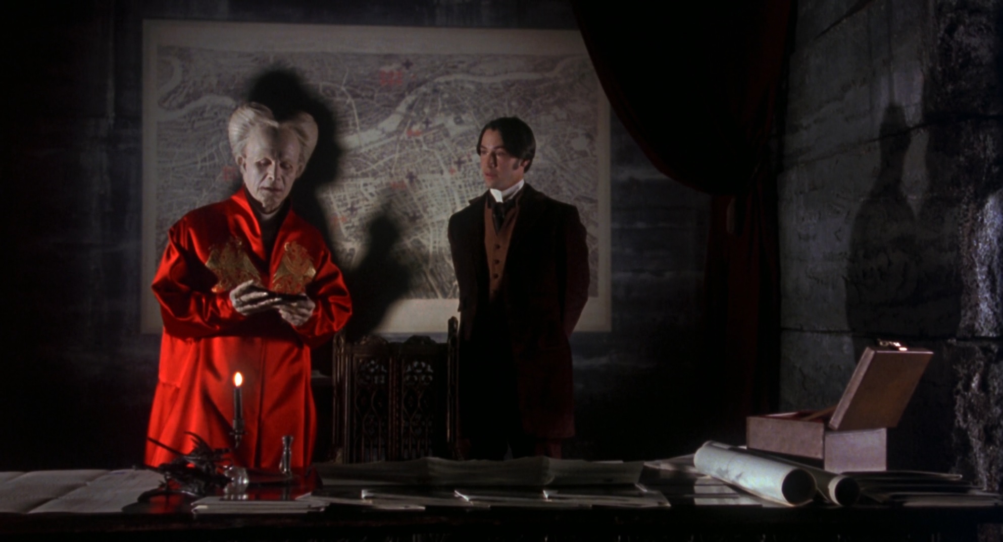 Cena do Filme Drácula de Bram Stoker mostrando o Conde Drácula em seu castelo ao lado do advogado Jonathan Harker. Drácula tem uma aparência singular, todo branco, com um cabelo também branco dividido ao meio e vestindo um robe vermelho muito brilhoso. Ele segura a foto de Mina Murray que pertence à Jonathan.
